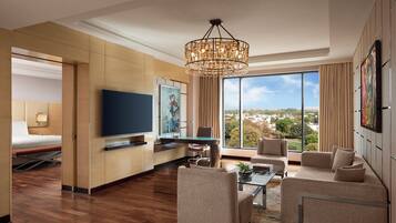 Una habitación de hotel moderna con una televisión de pantalla plana, zona de comedor, sofá y un amplio ventanal con vistas a la ciudad.