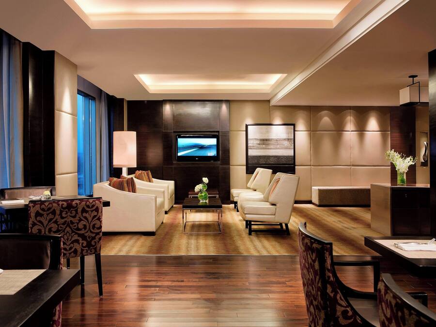 A modern hotel lobby with a flat-screen TV, comfortable seating, and a wooden floor.