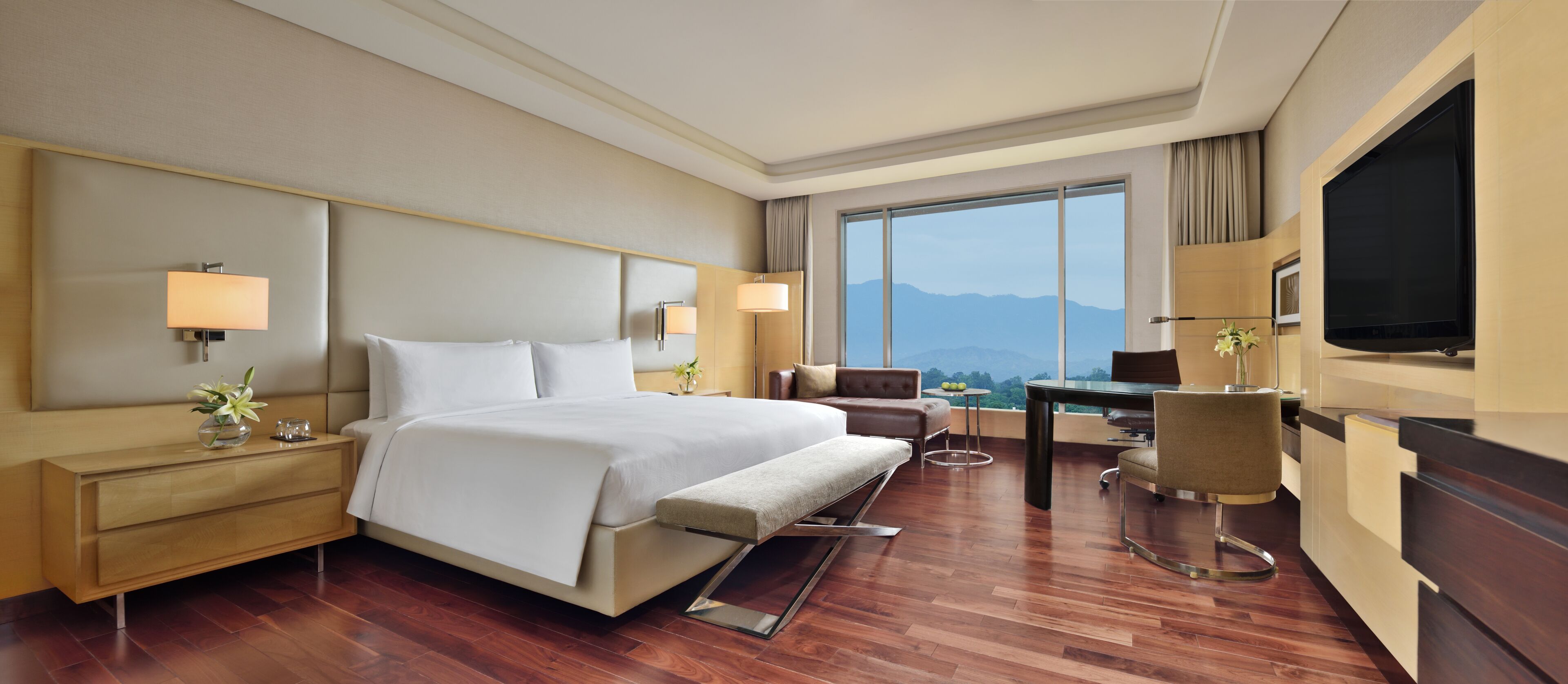 A modern hotel room with a large bed, a desk, a chair, and a TV.
