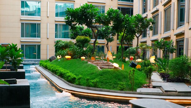 Un patio de hotel moderno con una fuente central, rodeado de follaje y zonas de estar.