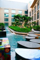 Un patio de hotel moderno con una fuente central, rodeado de follaje y zonas de estar.