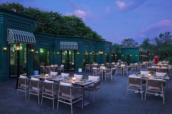An outdoor dining area with tables and chairs, a green building with awnings, and a red telephone booth.