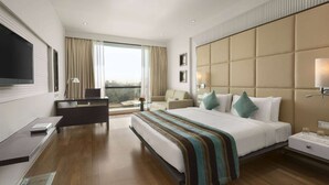 A modern hotel room with a large bed, a desk, a chair, a TV, and a window with a city view. - Ramada by Wyndham Navi Mumbai (Navi Mumbai)