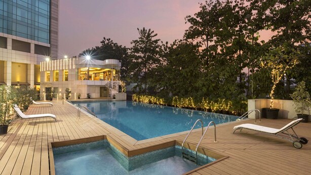 A rooftop pool area with a clear blue pool, wooden deck, and lounge chairs. - Ramada by Wyndham Navi Mumbai (Navi Mumbai)
