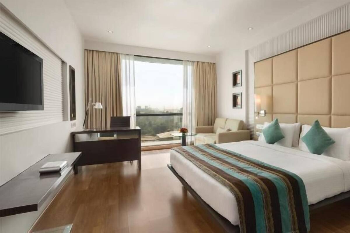 A hotel room with a large bed, a desk, a chair, a TV, and a window with curtains.