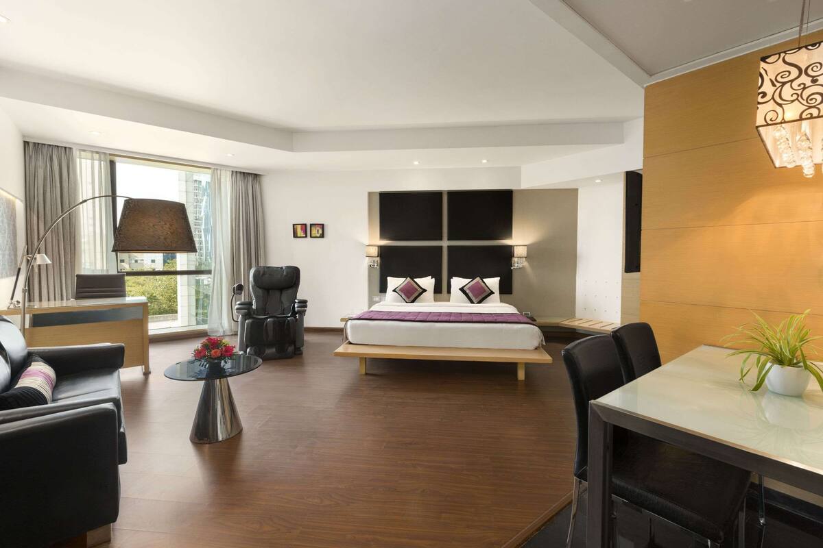 A modern hotel room with a bed, a desk, a chair, a table, and a large window.