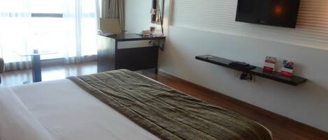 Habitación de hotel con cama, escritorio, televisor montado en la pared y ventana con cortinas.