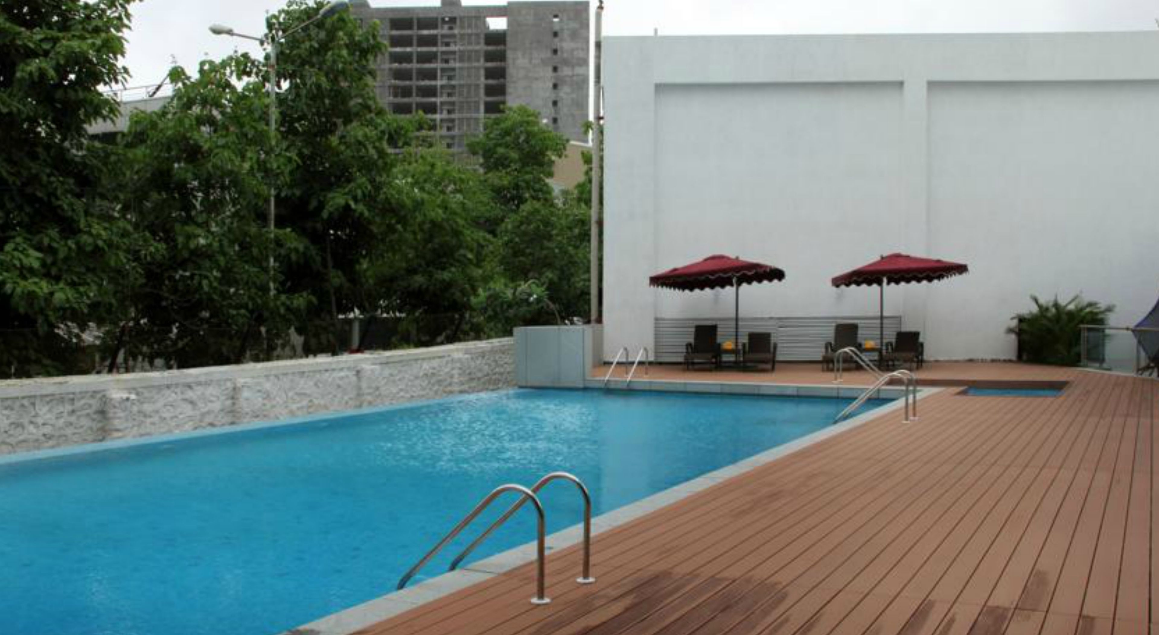A swimming pool with a wooden deck, two red umbrellas, and a seating area with chairs and a table.