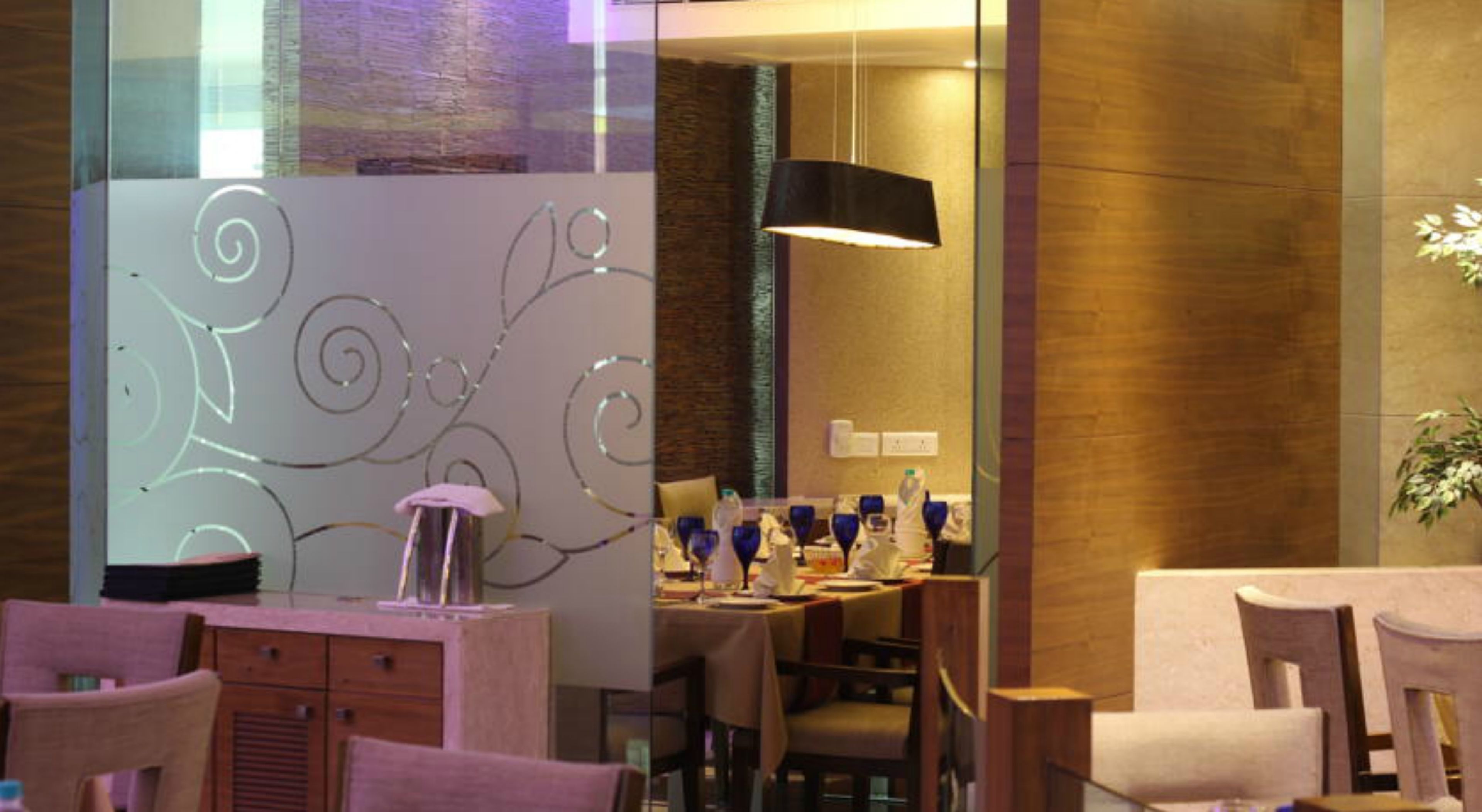 Un espace repas moderne doté d’une cloison en verre, de lambris en bois et d’un luminaire suspendu noir.