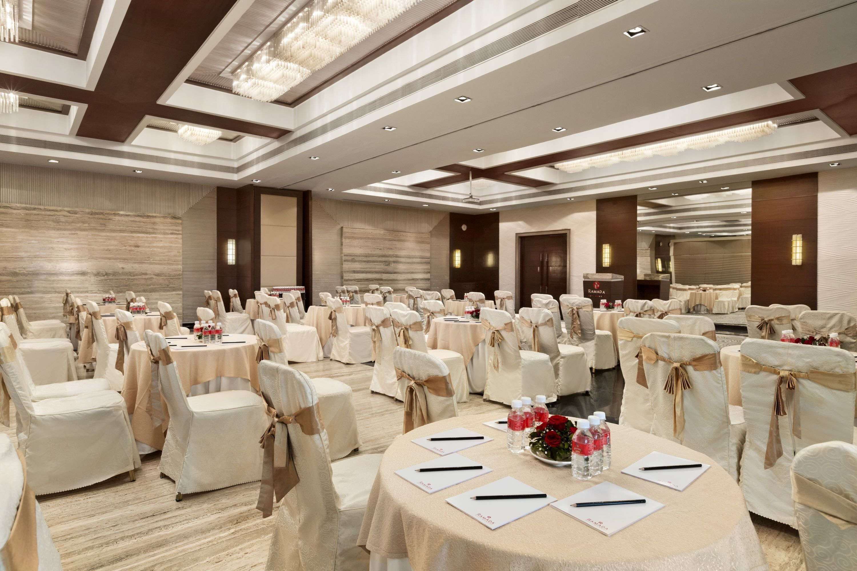 Un amplio salón de banquetes con mesas redondas, sillas y un techo alto con candelabros.