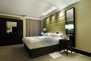 A hotel room with a large bed, a bedside table with a lamp, a mirror, and a wardrobe.