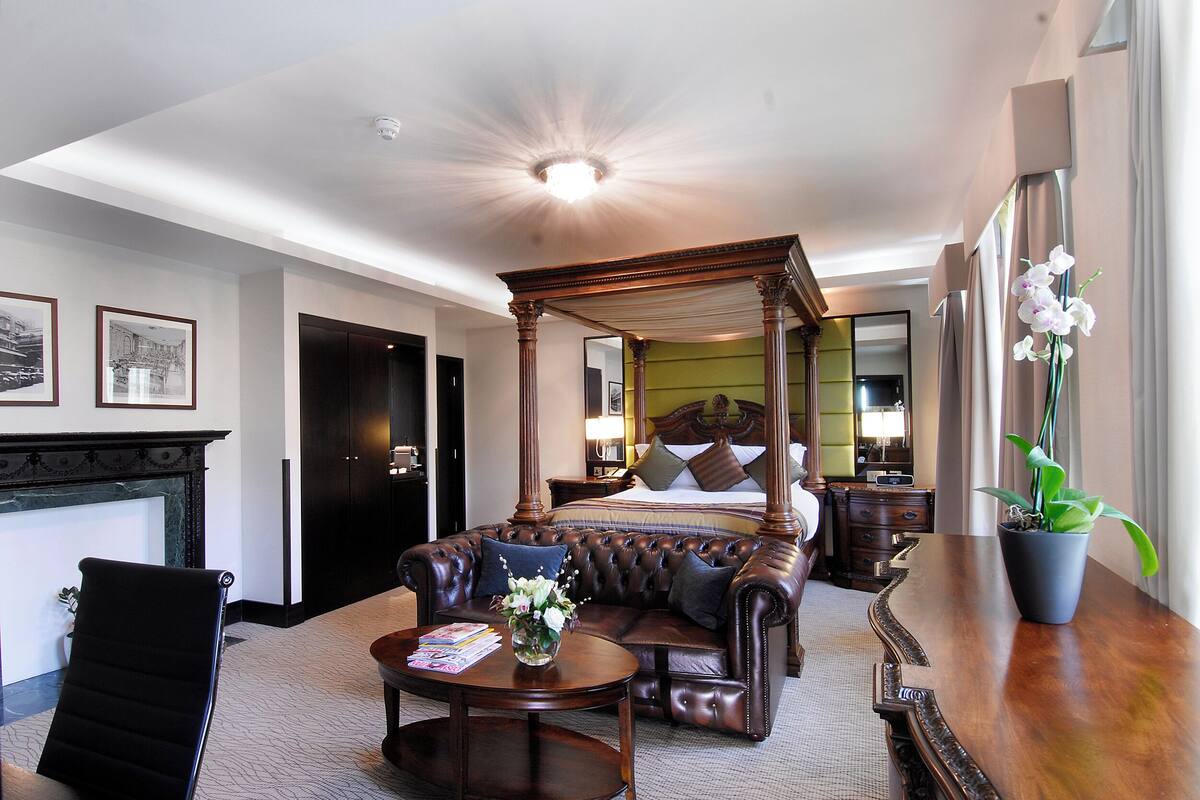Een hotelkamer met een hemelbed, een leren bank, een bijzettafeltje en een potplant.