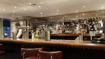 A bar area with a wooden counter, multiple liquor bottles, and two leather bar stools.