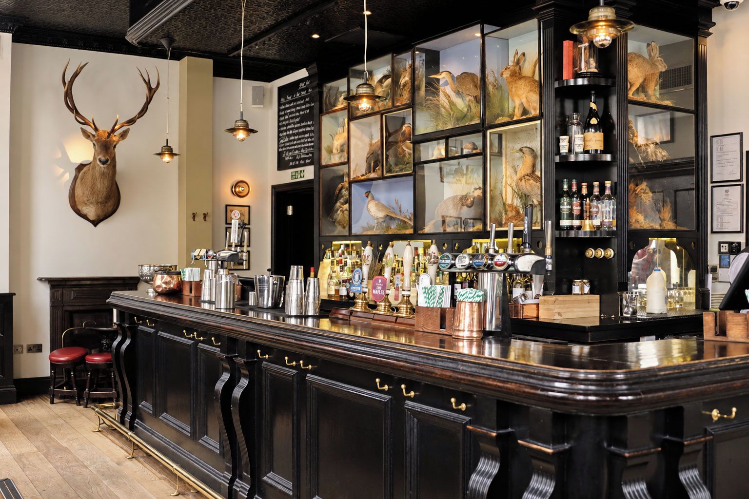 A bar area with a counter, stools, and a variety of bottles and glasses.