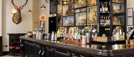 A bar area with a counter, stools, and a variety of bottles and glasses.