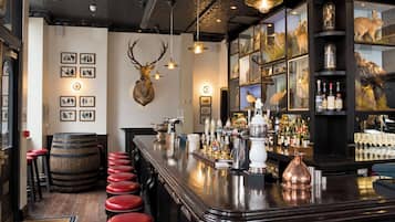 Eine Bar mit Holztresen, roten Barhocker, einem aufgehängten Hirschgeweih und einer Weinauslage.