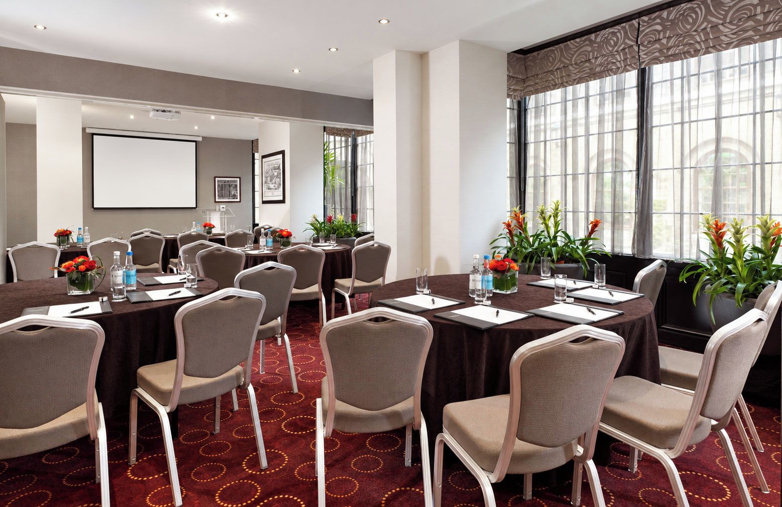 A conference room with round tables, chairs, and a projector screen.