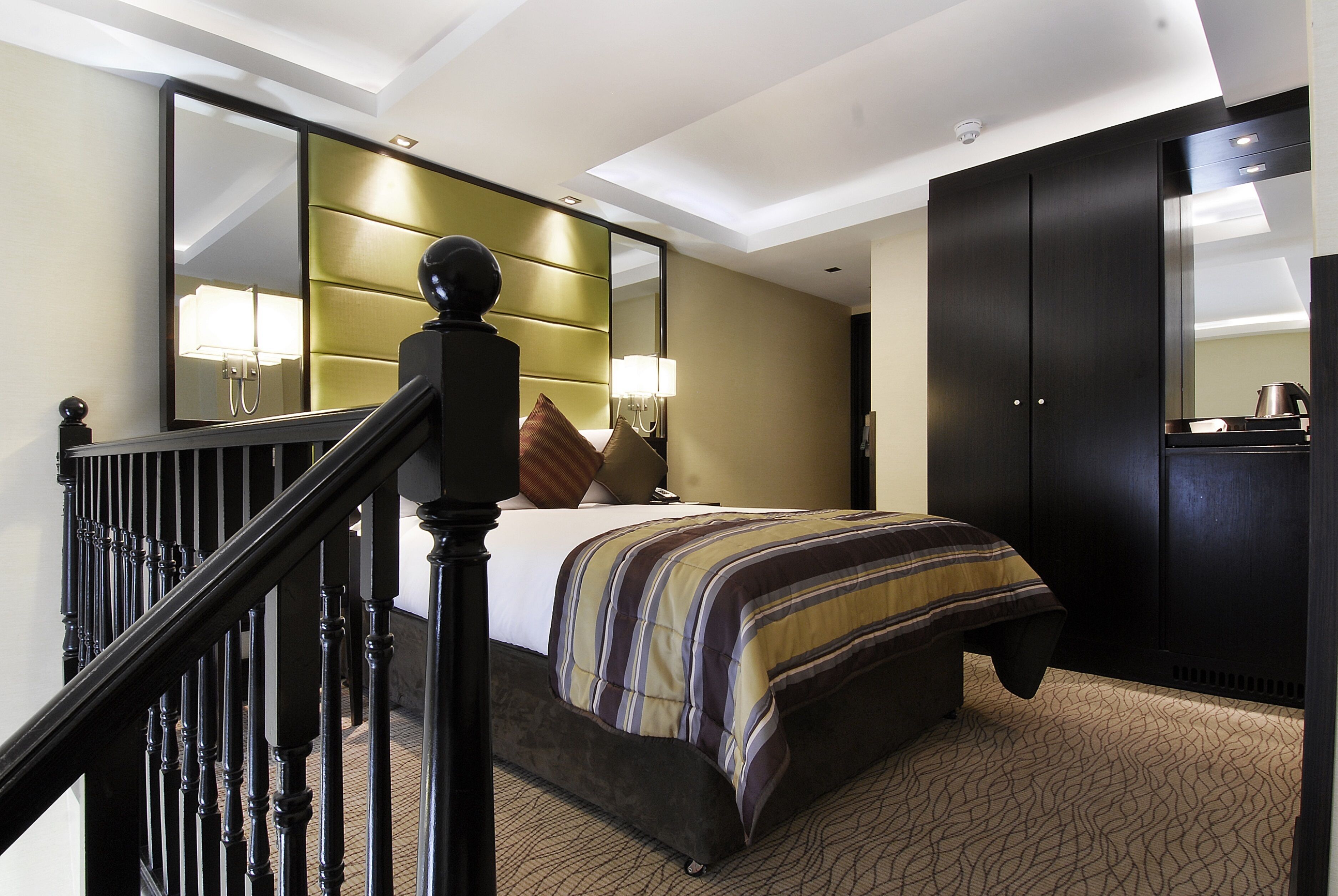A hotel room with a bed, a large mirror, a wardrobe, and a staircase.