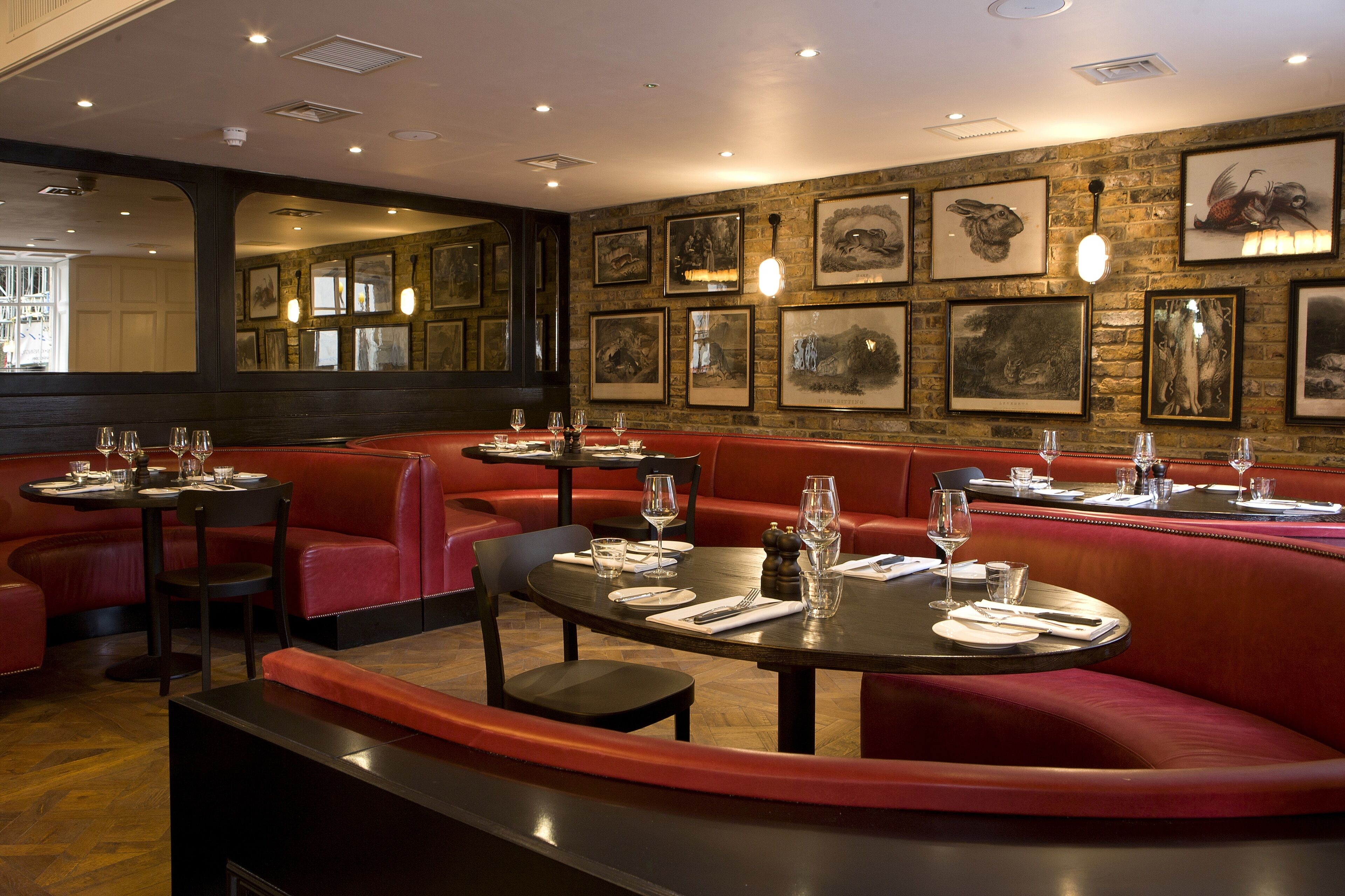A restaurant interior with red booths, round tables, and framed artwork on the walls.