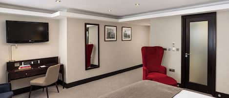 A hotel room with a bed, a desk, a chair, a TV, and a door.