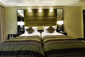 Ein Hotelzimmer mit einem großen Bett, zwei Nachttischen mit Lampen, einem Spiegel und einer Uhr.
