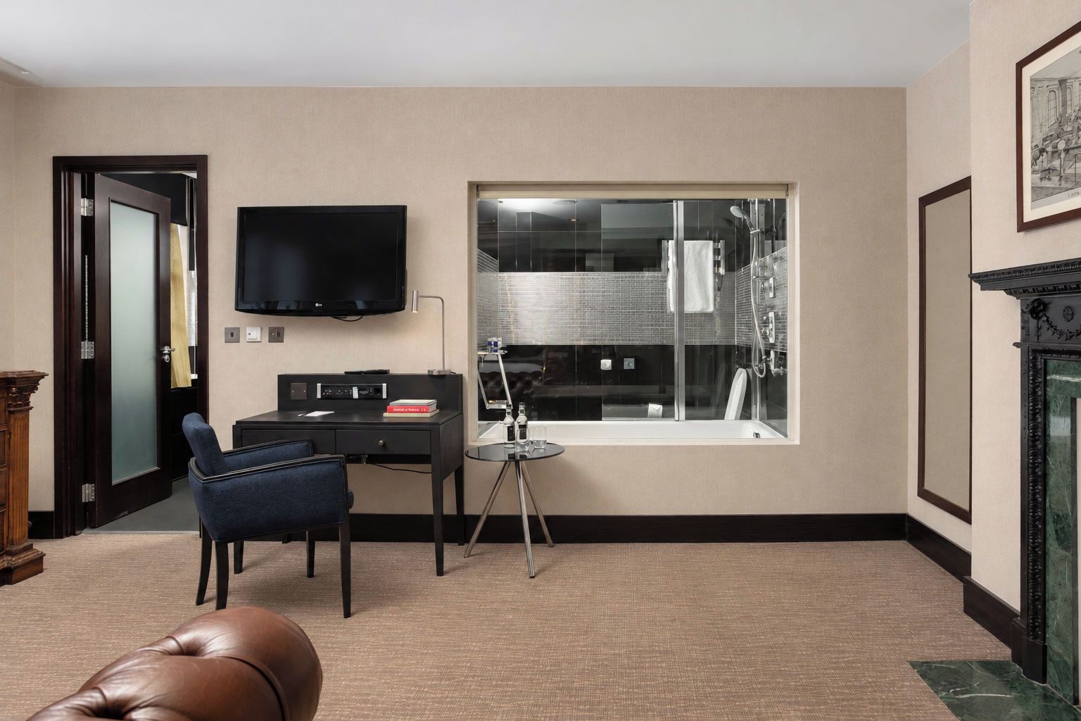 A hotel room with a desk, chair, television, and a large window.