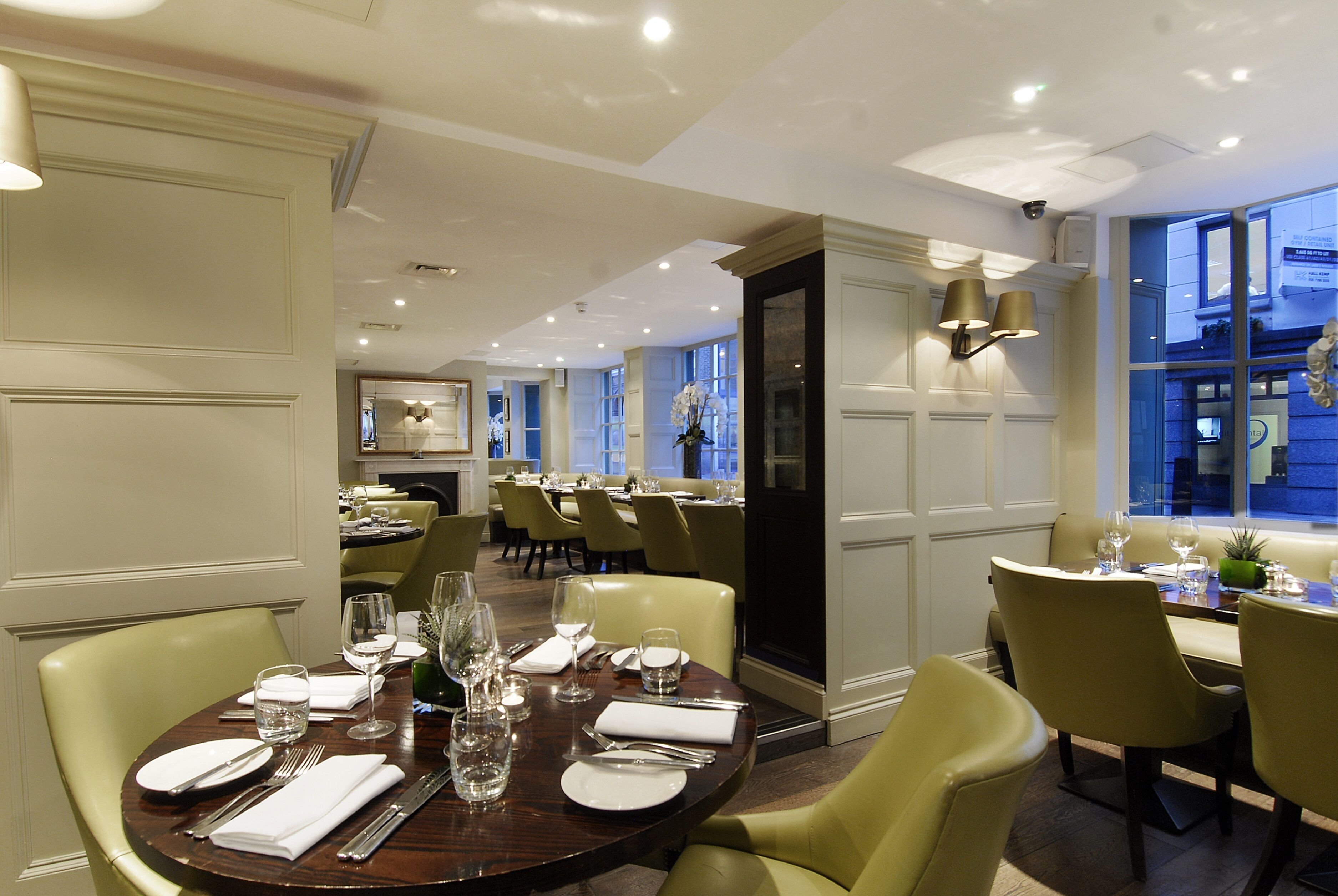 Une salle à manger bien éclairée, avec des tables rondes, des chaises et un lustre moderne.
