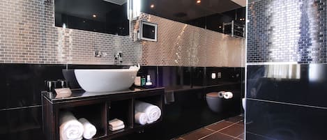 Een moderne badkamer met een grote witte wastafel, een donker houten wastafelmeubel en zwarte betegelde wanden.