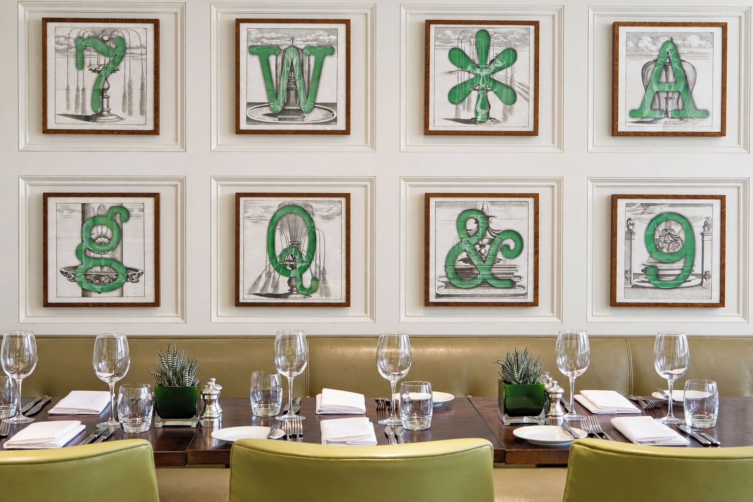 Un coin repas avec une table dressée pour six personnes, des œuvres d’art encadrées accrochées au mur et une plante verte posée sur la table.