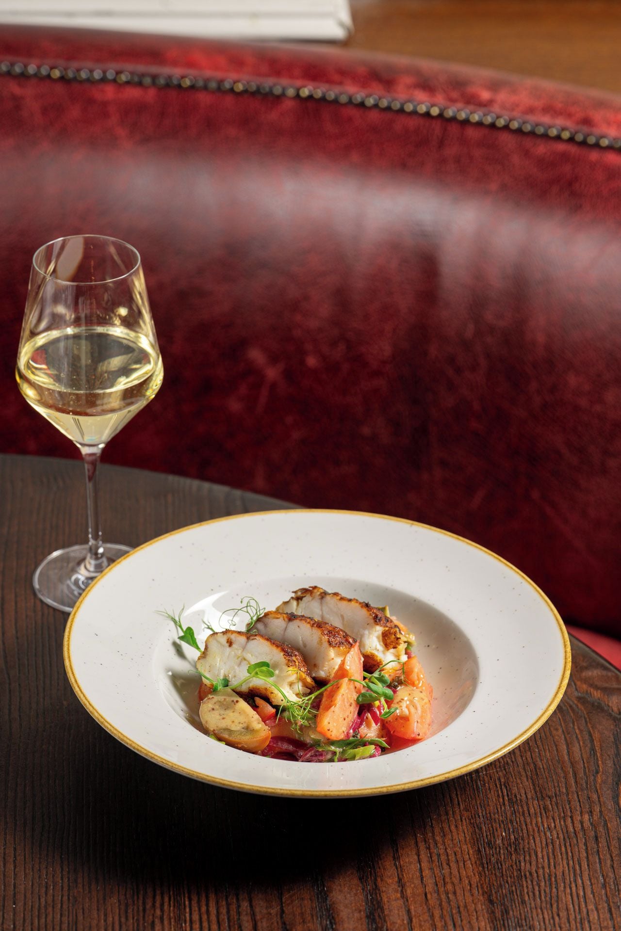 A plate of food with a glass of white wine on a wooden table.