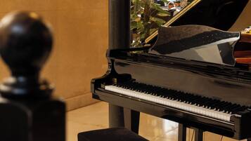 A grand piano with a bench in a room with a tiled floor and a plant in the background.