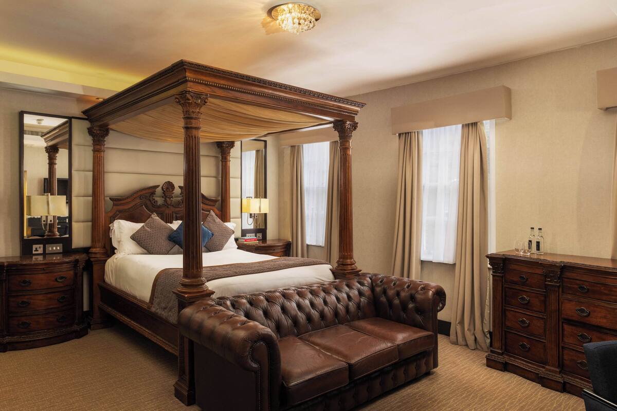 Een hemelbed met een gestoffeerde leren bank, houten nachtkastjes en een dressingkast.