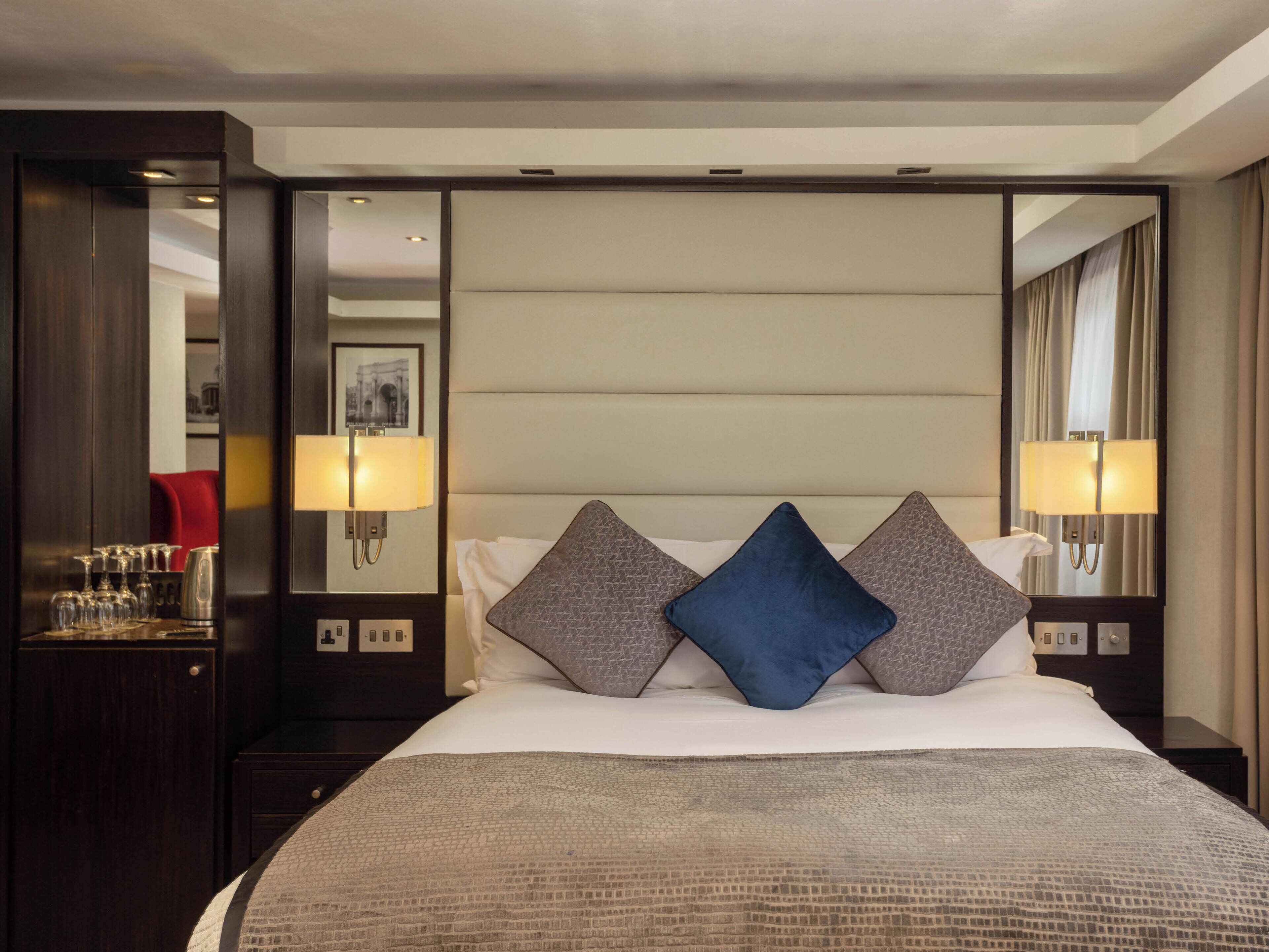 Une chambre d’hôtel avec un grand lit, deux oreillers, une table de chevet, un miroir et une lampe fixée au mur.