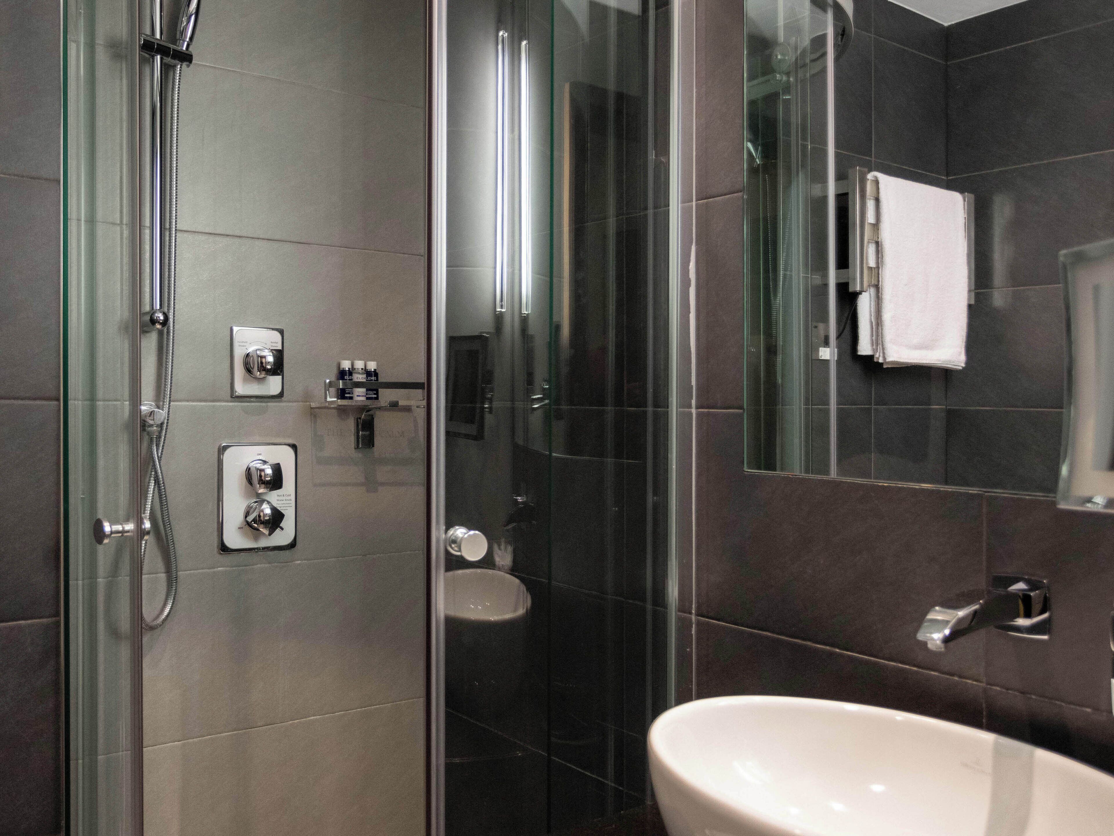 A modern bathroom with a glass-enclosed shower, a white sink, and dark tiled walls.