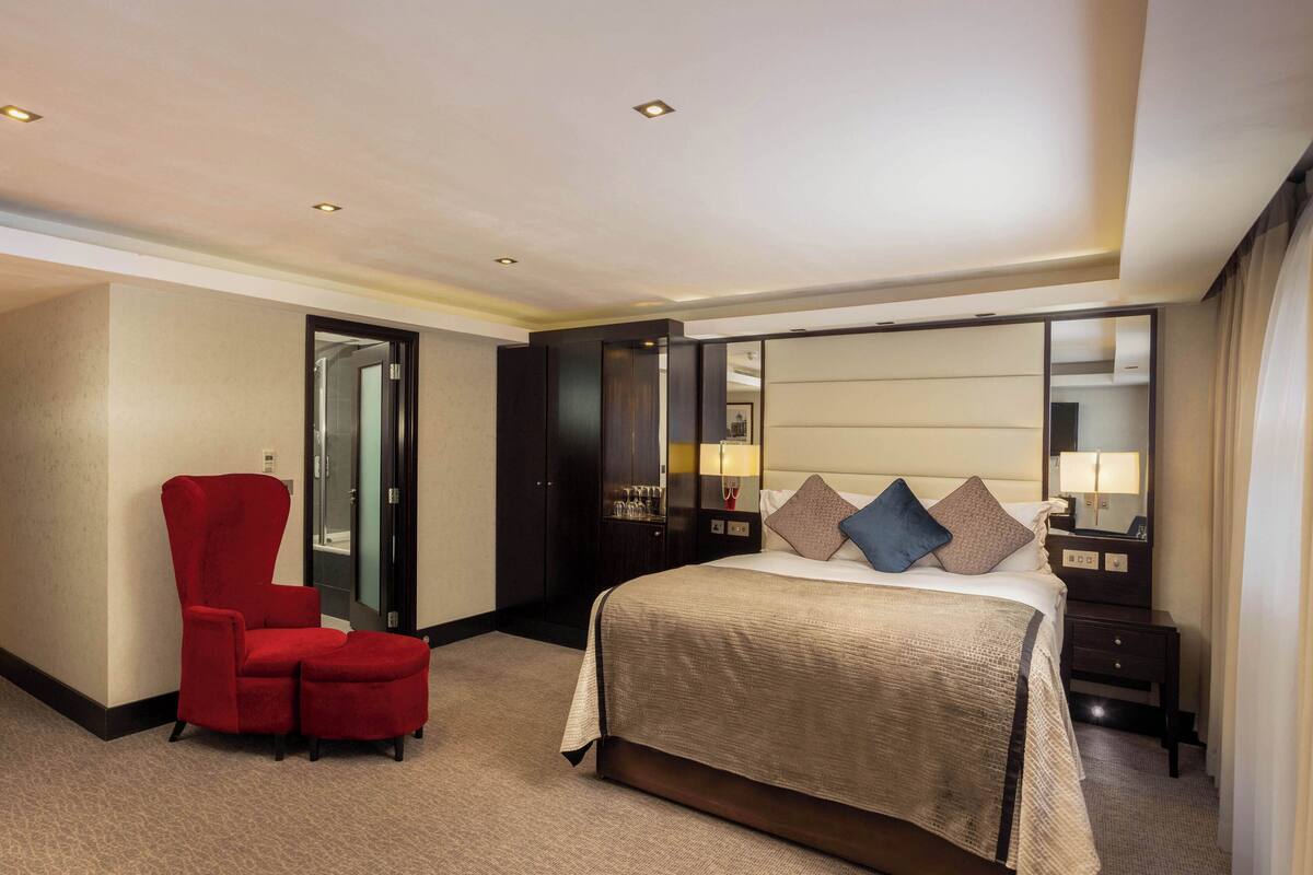 Een hotelkamer met een groot bed, een rode fauteuil, een kledingkast en een spiegel.