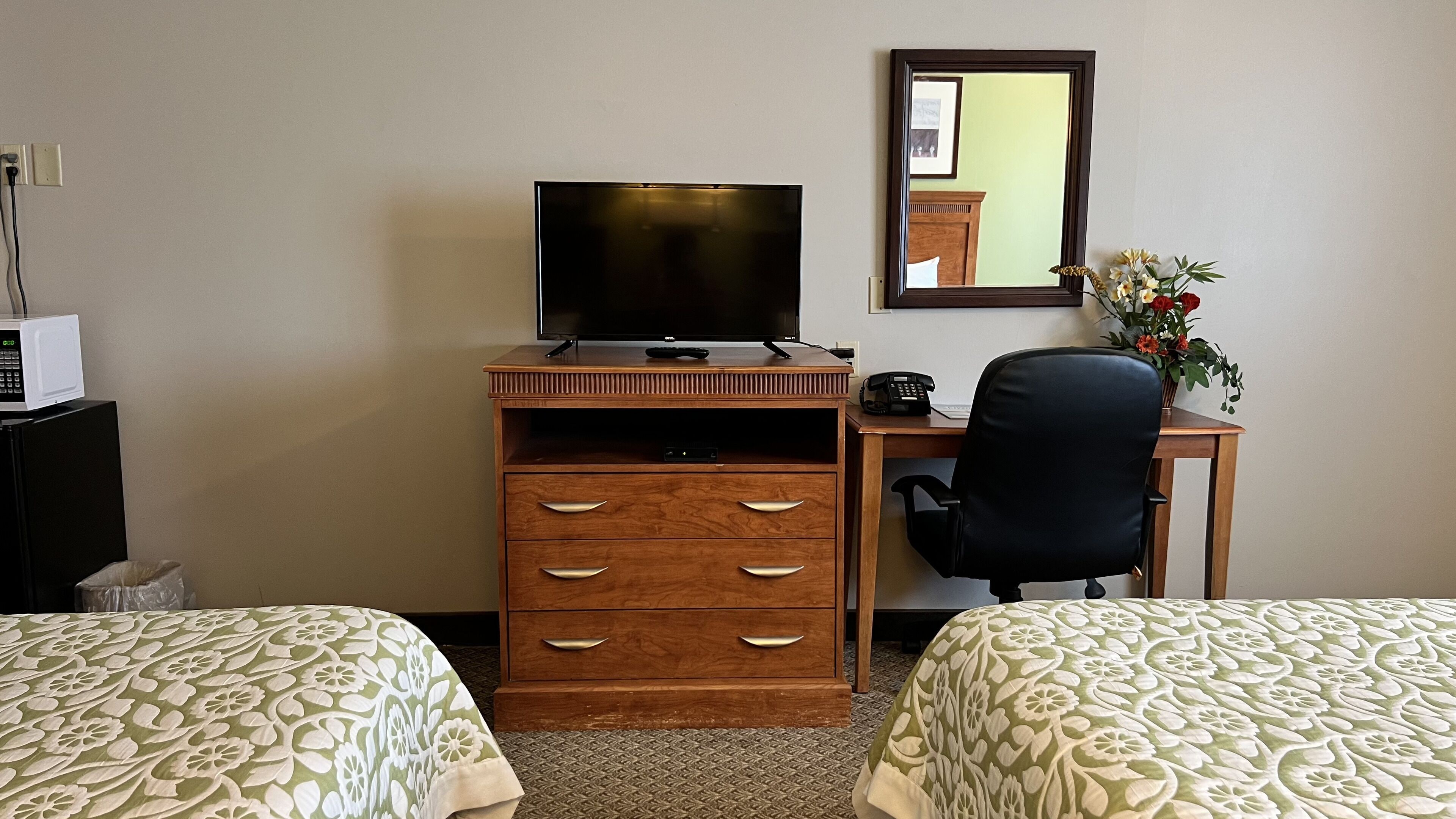 Ein Hotelzimmer mit zwei Betten, einem Schreibtisch mit Computer, einem Fernseher, einem Telefon und einem Spiegel.