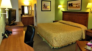 Habitación de hotel con una cama, un escritorio con televisor, una silla, una lámpara de escritorio y dos lámparas de pared.