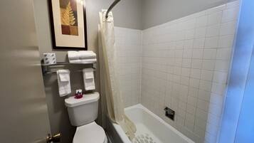 A bathroom with a toilet, a shower with a curtain, and a shelf with towels and toiletries.