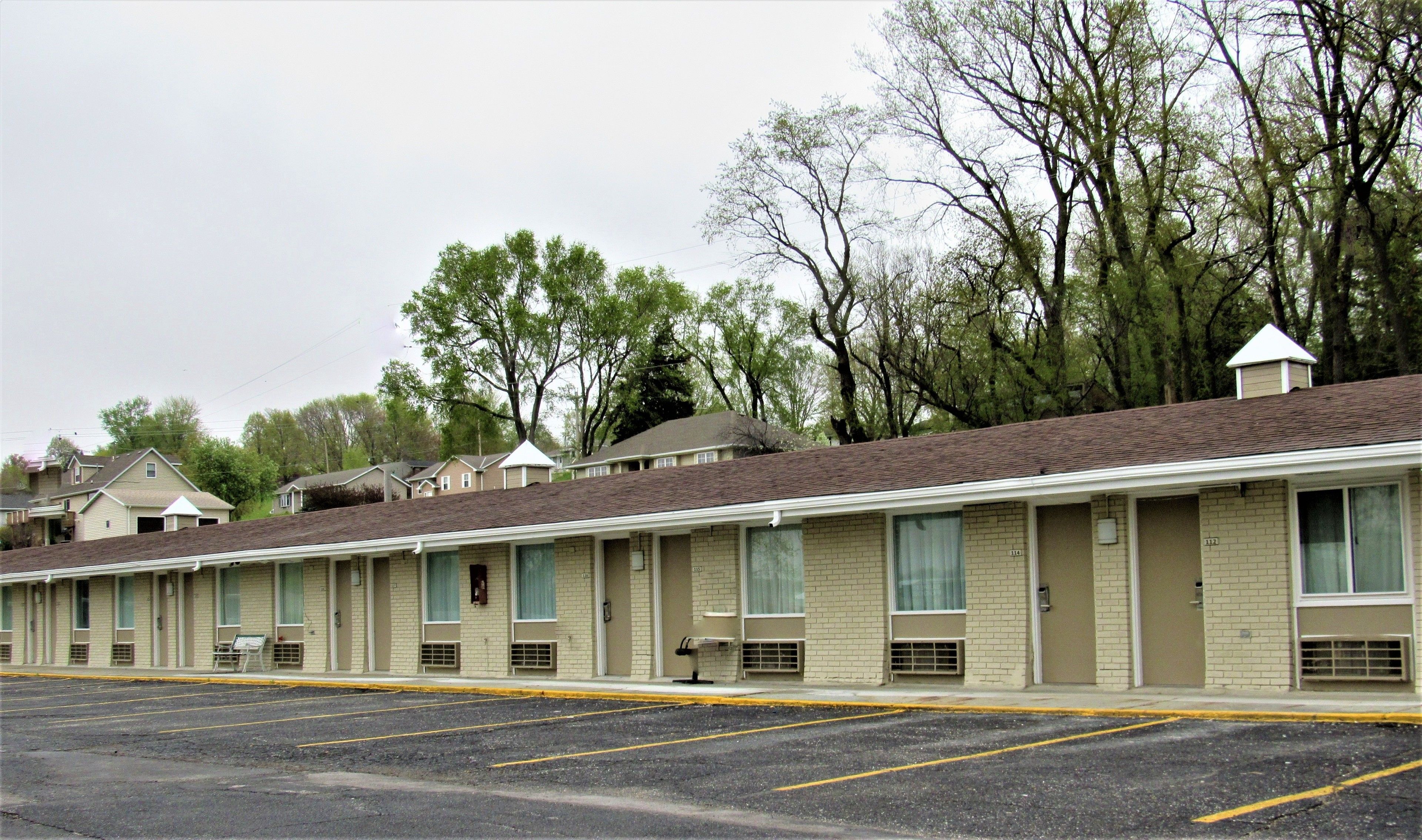 Une rangée de bâtiments d’un motel, avec des chambres individuelles, un parking et des arbres en arrière-plan.