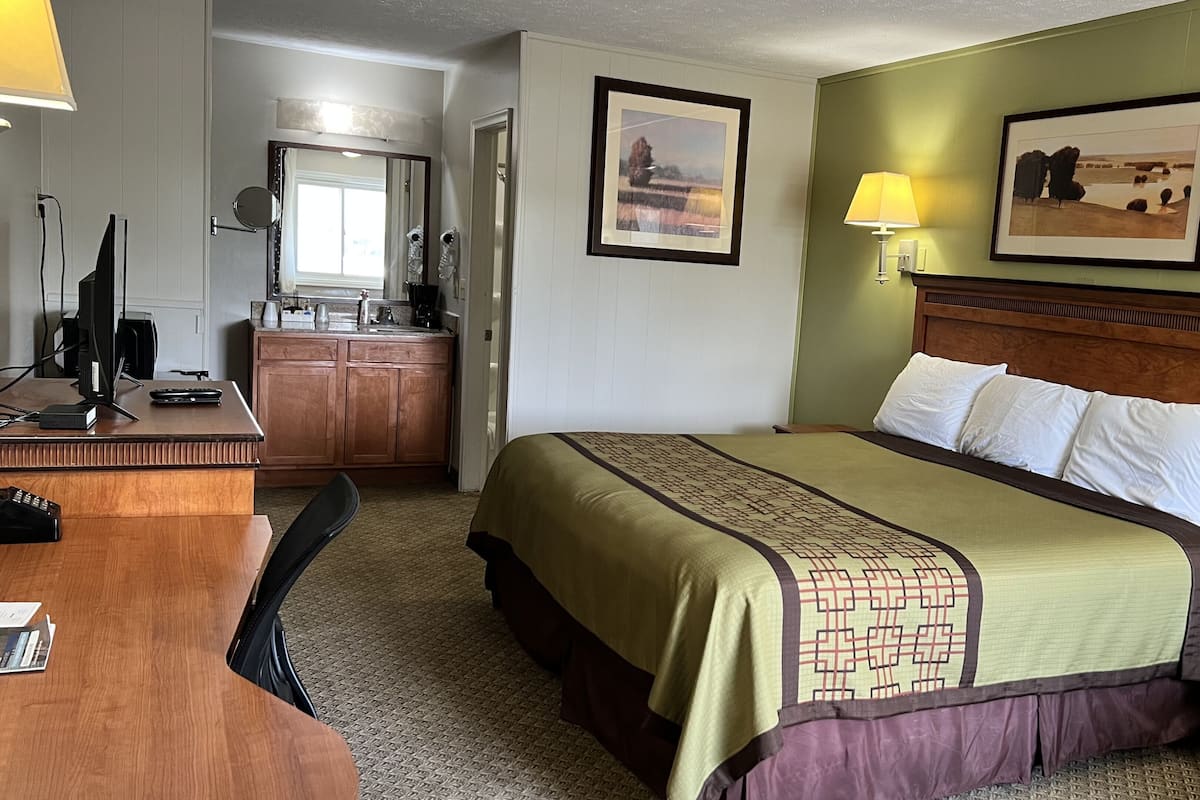 Quarto de hotel com cama, escrivaninha com computador, espelho e pia.