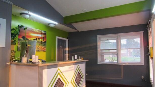 Una habitación con mostrador de recepción, un cuadro de un atardecer, una ventana con persianas y una pared verde.