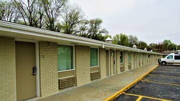 A row of motel rooms with individual doors, a parking lot, and a white van parked in the lot.