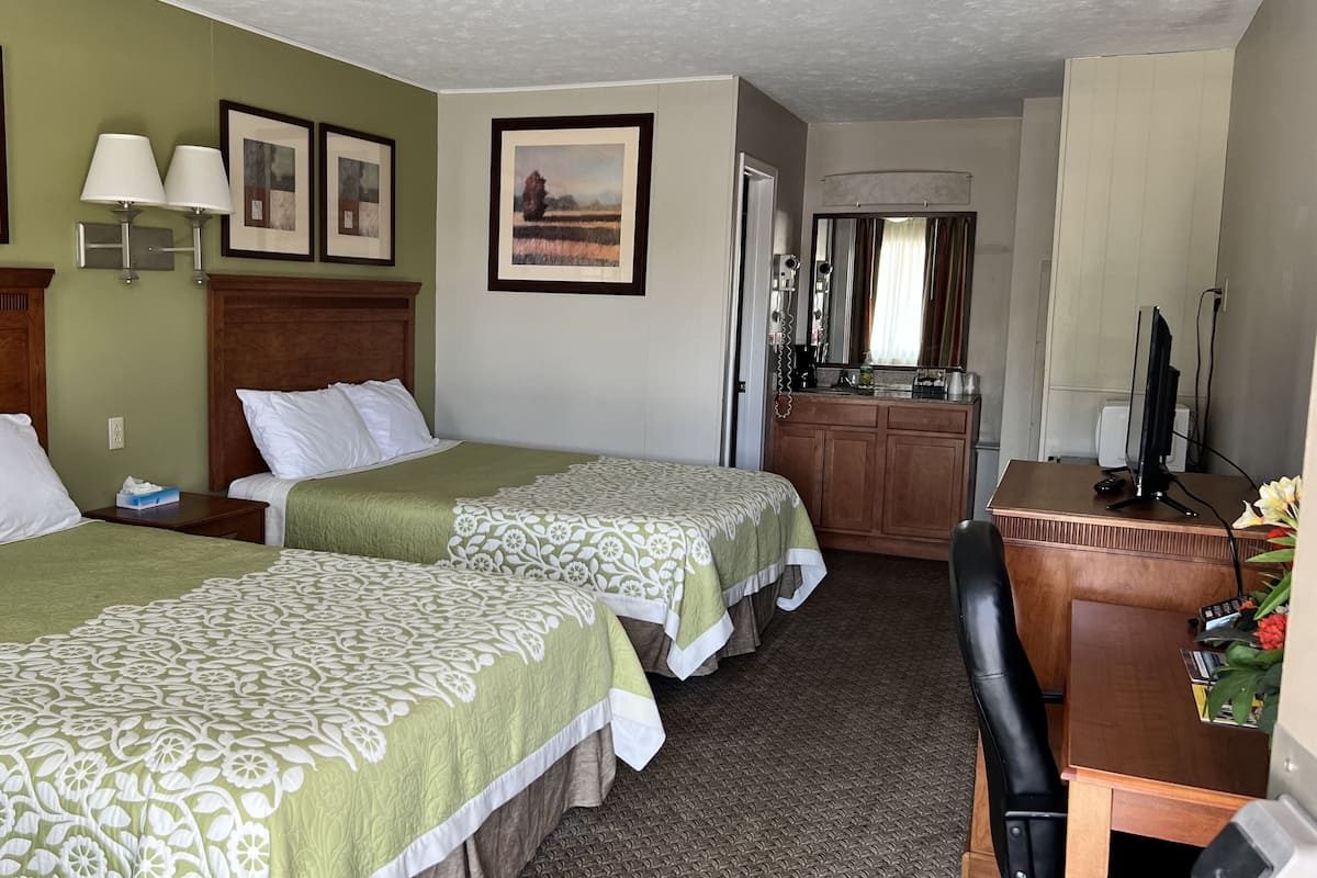 Quarto de hotel com duas camas, uma cabeceira de madeira, uma mesa de trabalho com computador e um espelho.