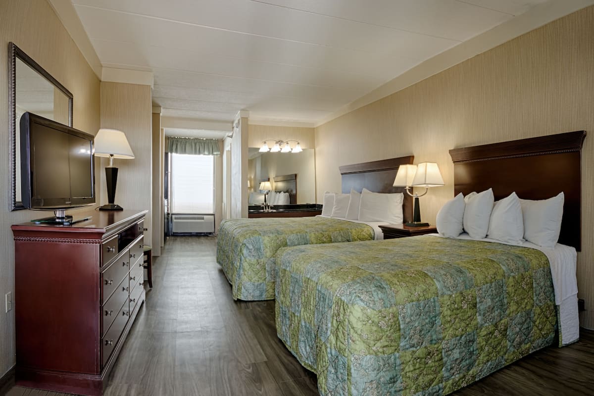A hotel room with two beds, a TV, a dresser, and a bathroom visible through an open door.