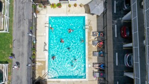 An aerial view of a swimming pool surrounded by lounge chairs and umbrellas, with a parking area adjacent to it. - The Barefoot Mailman (Ocean City)