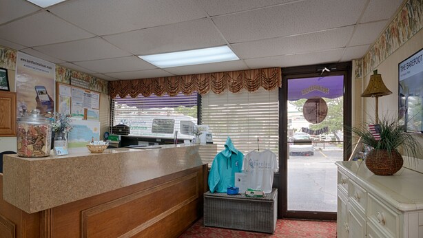 A reception area with a wooden reception desk, a wicker basket, a blue jacket, and a white cabinet with a pineapple on top. - The Barefoot Mailman (Ocean City)