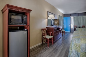 A hotel room with a bed, a desk with a computer, a microwave, and a refrigerator.