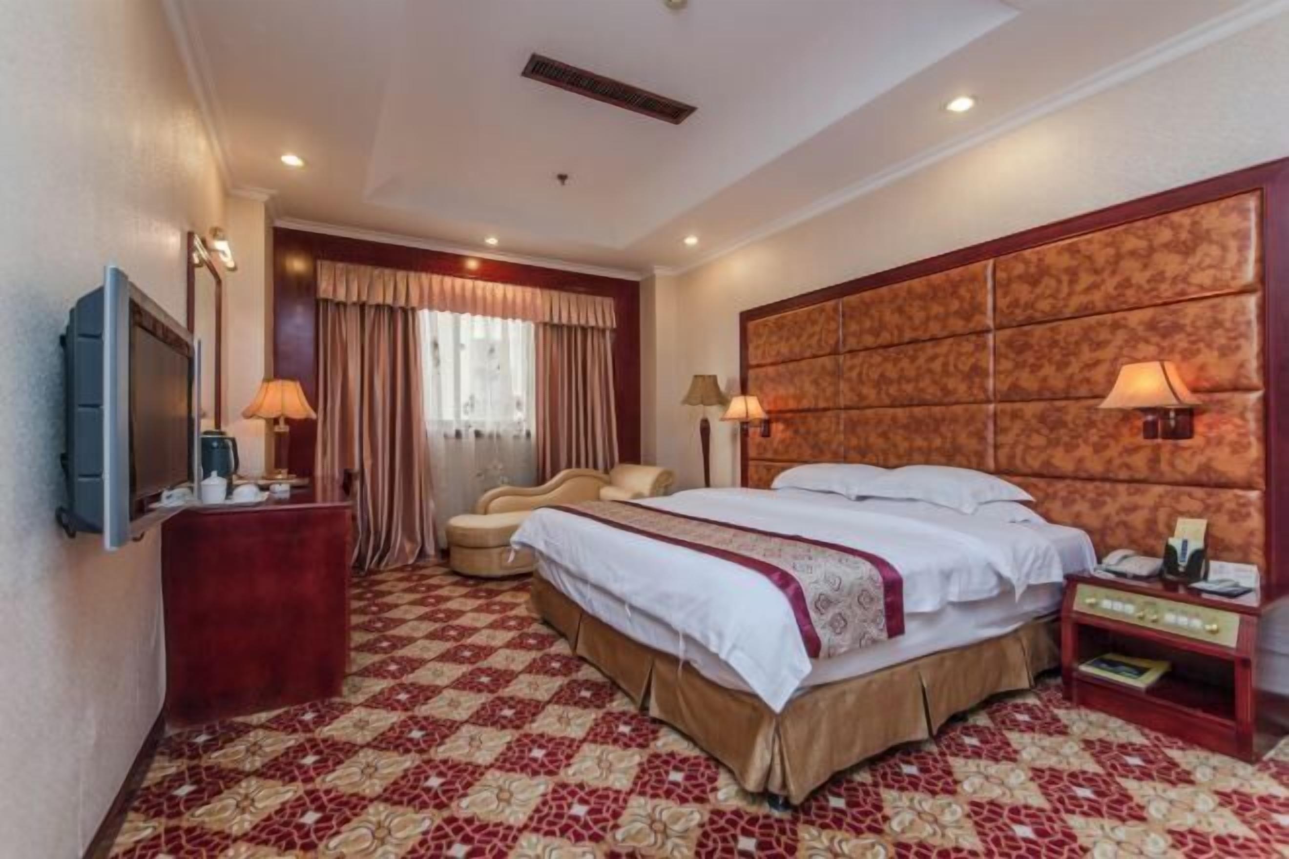 A hotel room with a large bed, a TV, a desk, and a chair.