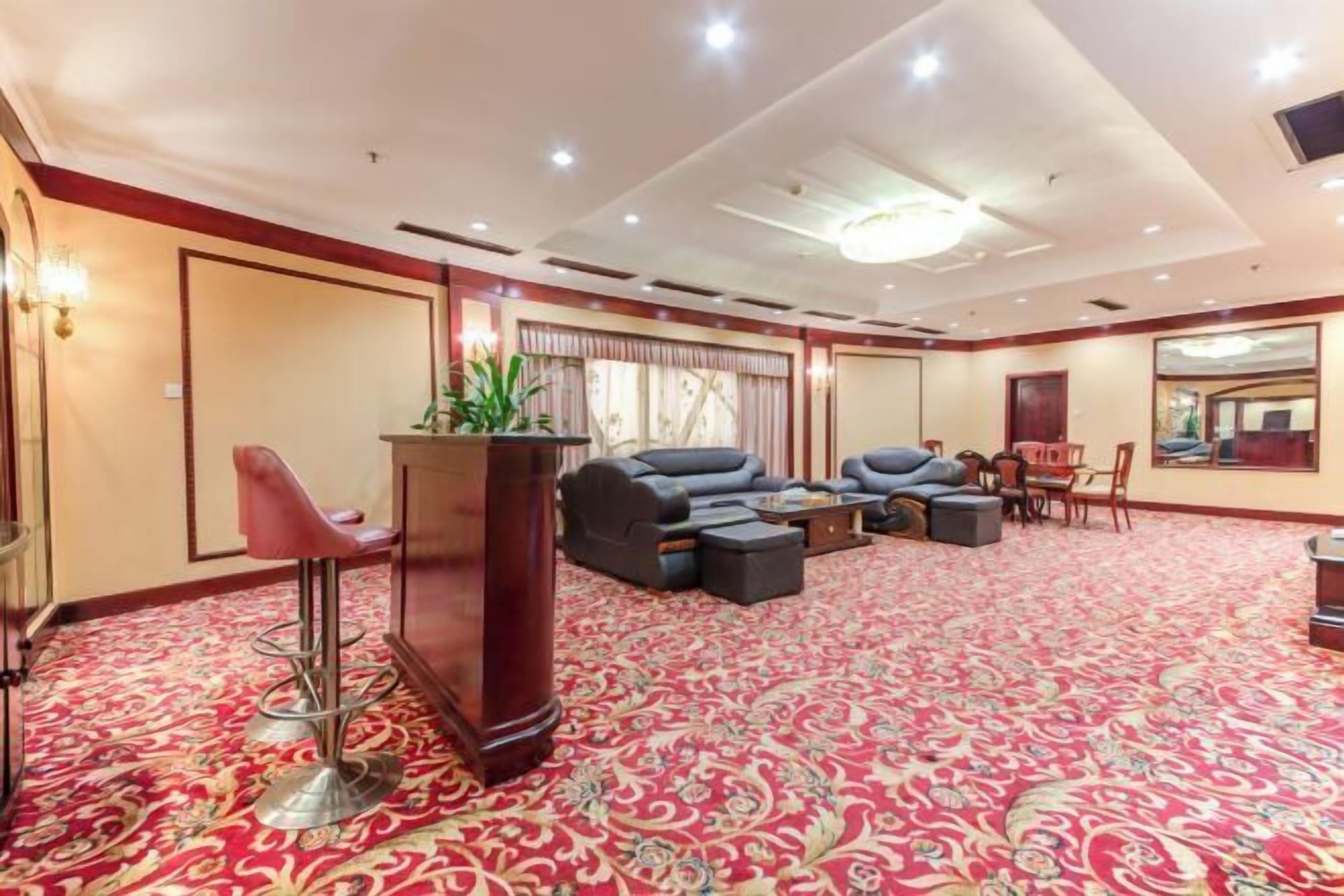 A spacious room with a red carpet, a bar area with stools, a sofa set, and a large mirror.