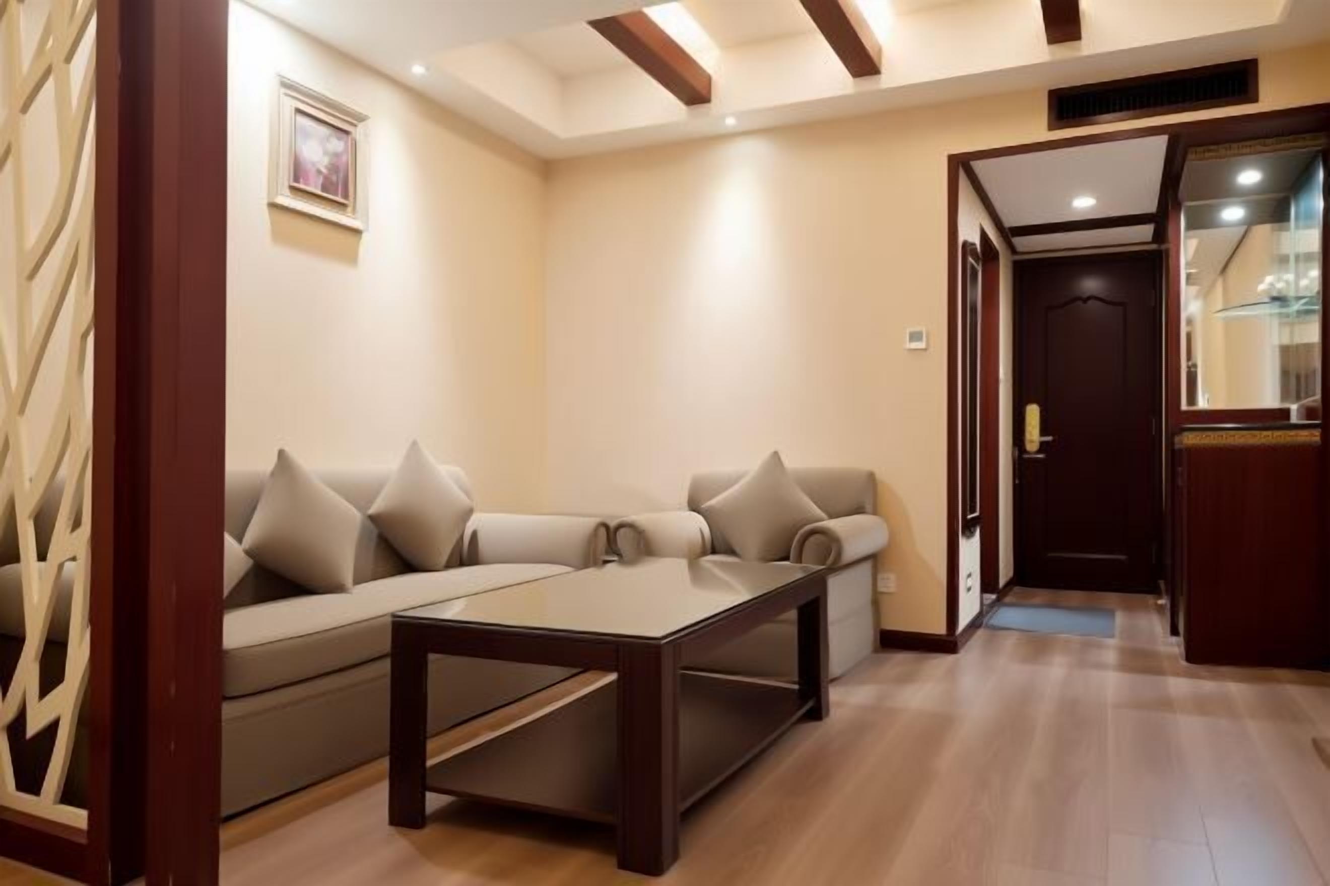 A living room with a sofa, a coffee table, wooden flooring, and a door leading to another room. - Temeisi Hotel (Jieyang)